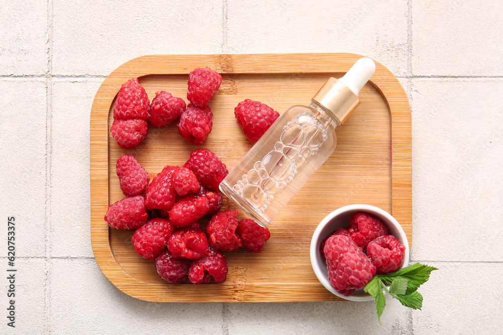 Wooden board with bottle of cosmetic raspberry oil on white tile background