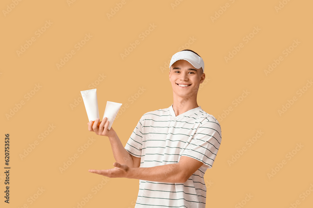 Happy young man with bottles of sunscreen cream on orange background