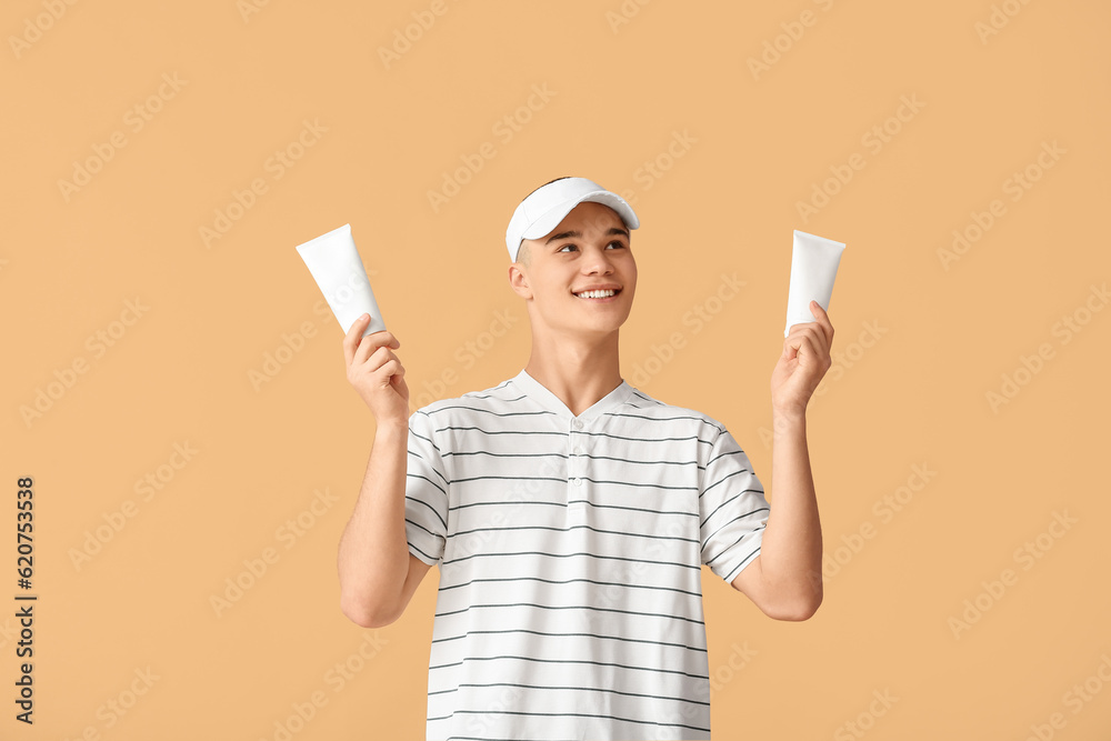 Happy young man with bottles of sunscreen cream on orange background