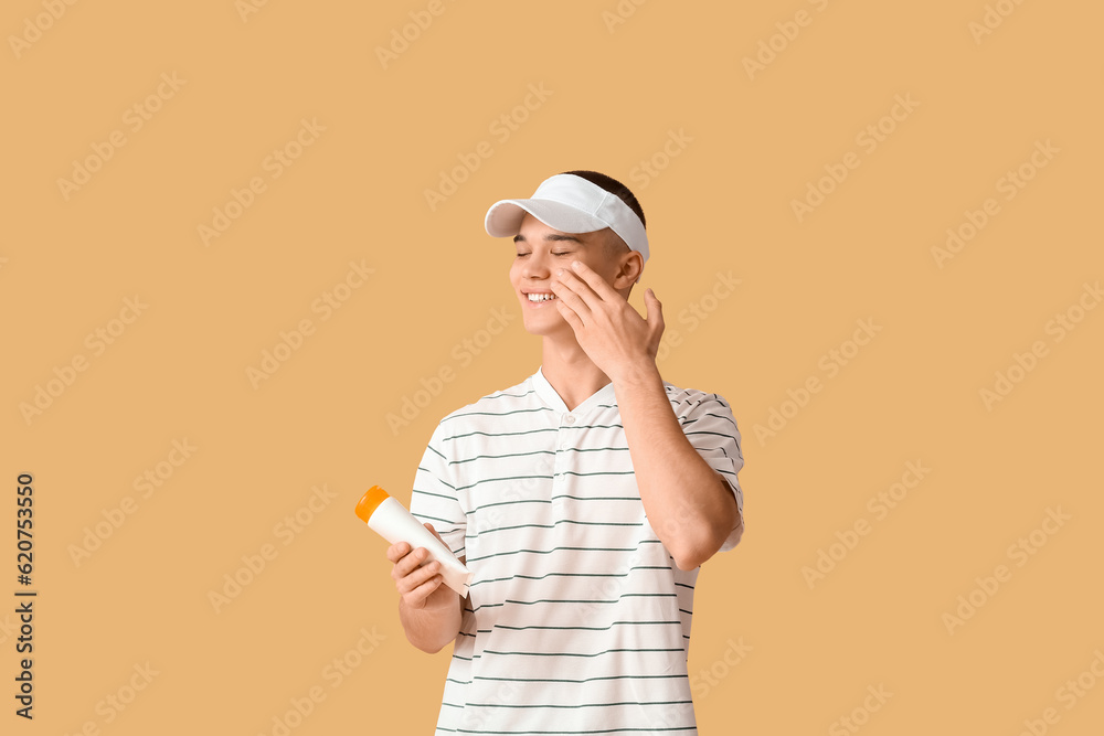 Happy young man applying sunscreen cream on orange background