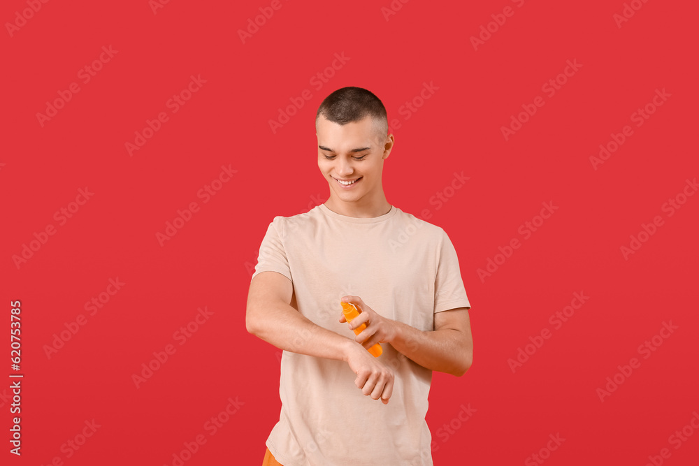 Happy young man applying sunscreen cream on his body against red background