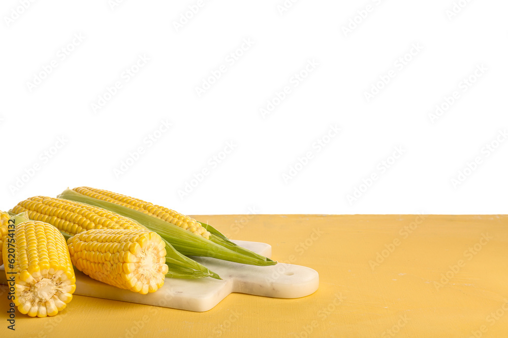 Board with fresh corn cobs on yellow table against white background