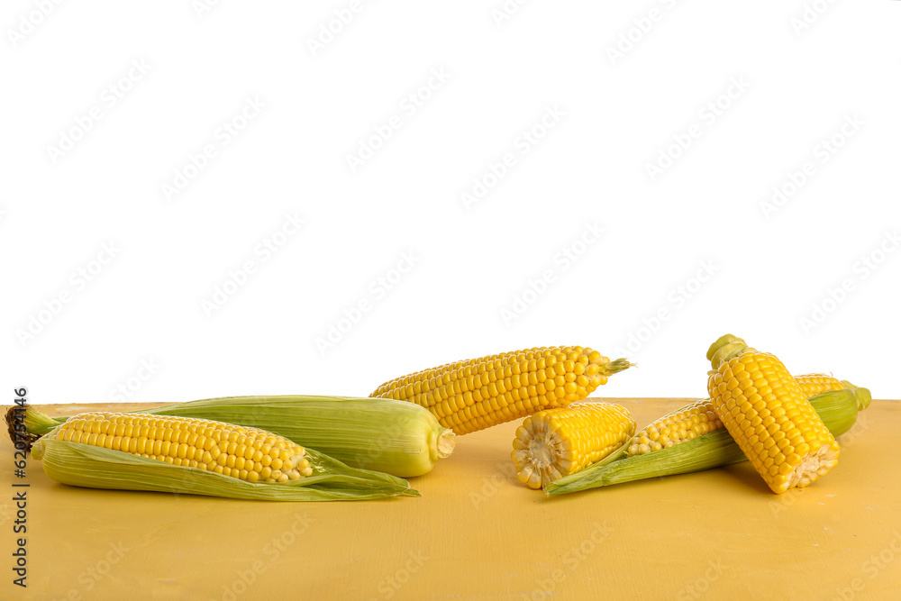 Fresh corn cobs on yellow table against white background