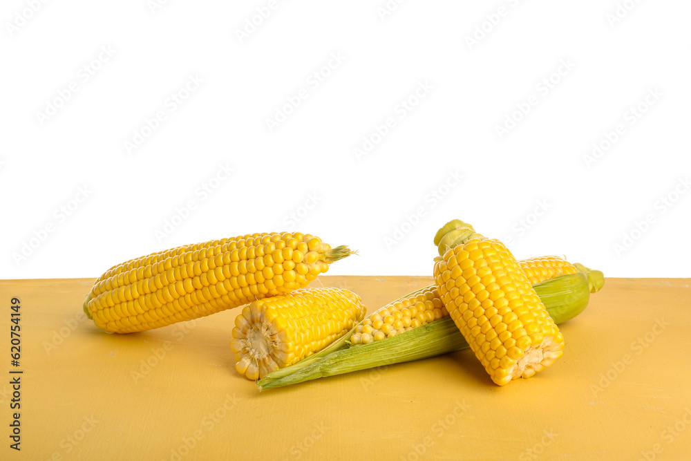 Fresh corn cobs on yellow table against white background