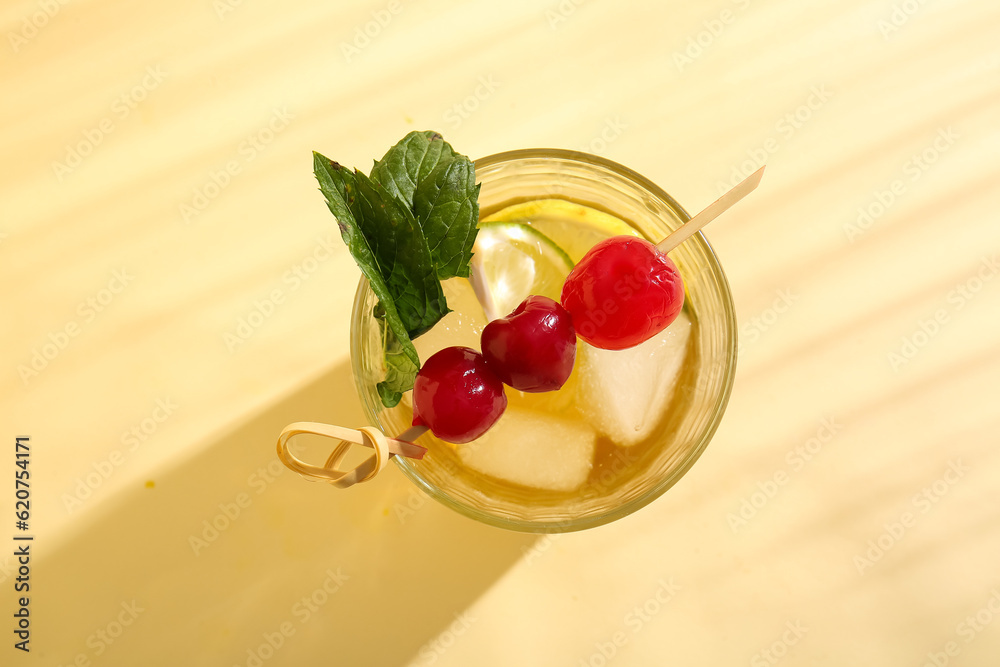 Glass of tasty cocktail with maraschino cherries on yellow background