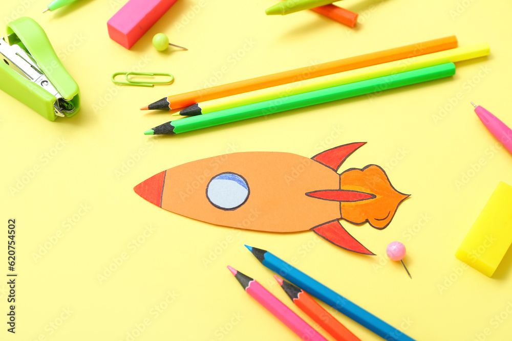 Paper rocket with school stationery on yellow background