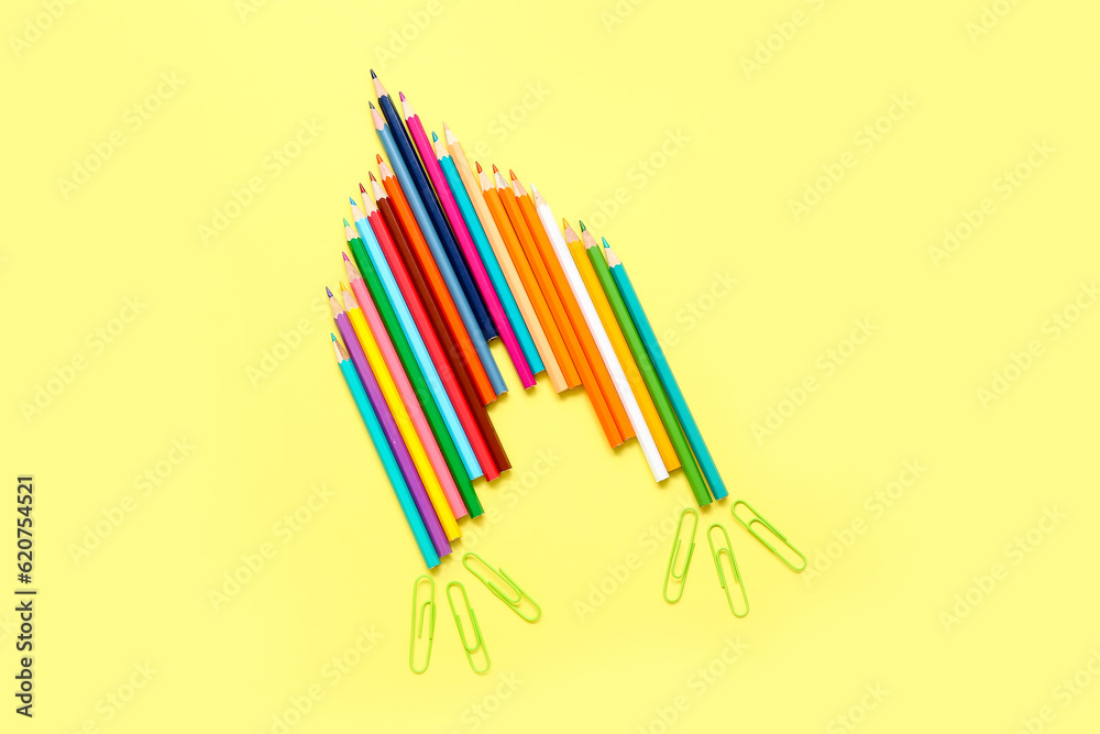 Pencils and paper clips in shape of rocket on yellow background