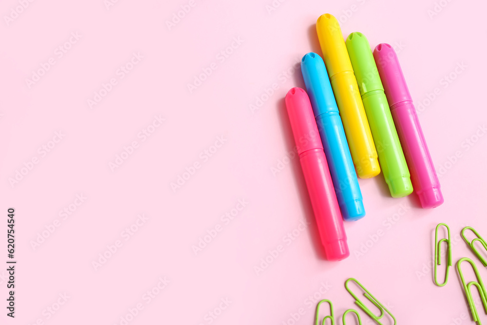 Markers and paper clips in shape of rocket on pink background