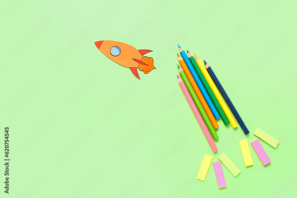 Pencils and stickers with paper rocket on green background