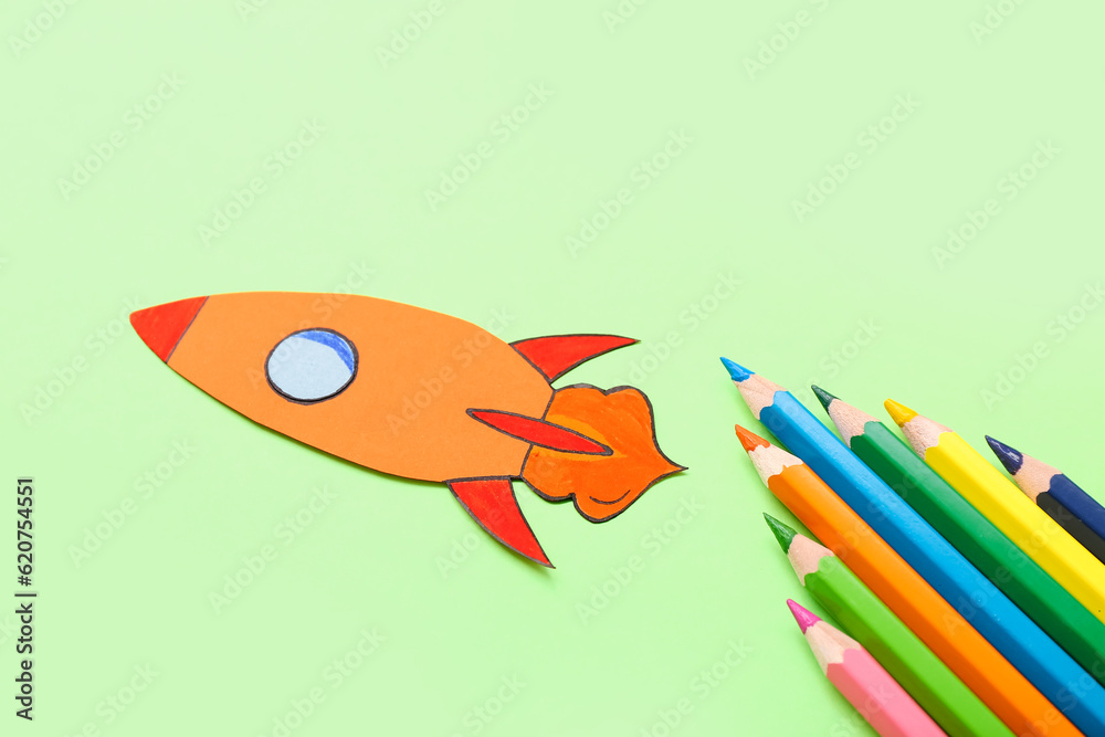 Pencils with paper rocket on green background