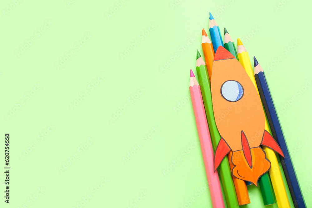 Pencils with paper rocket on green background