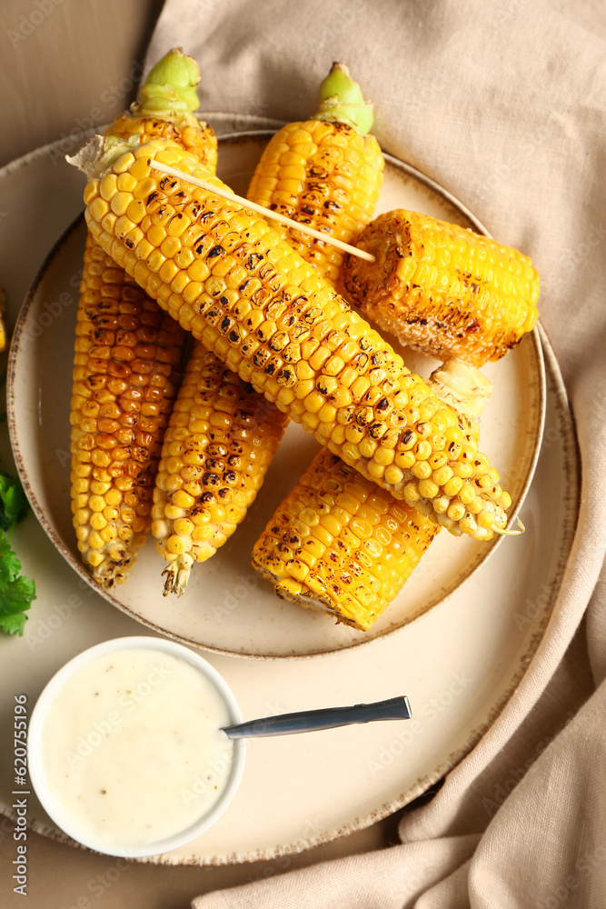 Plate with tasty grilled corn cobs and sauce on brown background