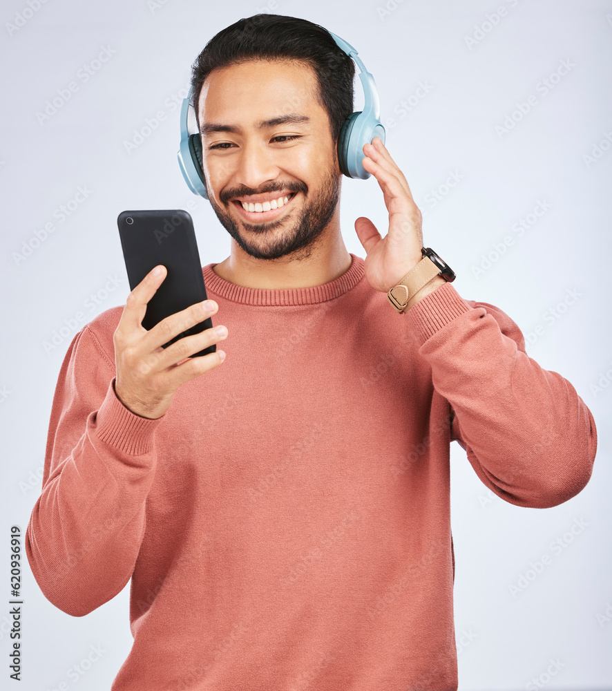 Man, headphones and smartphone for music in studio, white background and podcast app. Happy asian ma