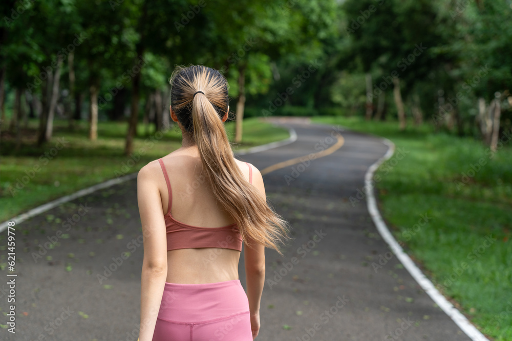 Back view of a long hair woman in fitness clothes walking in the morning during her morning run at  