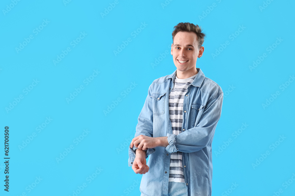 Young man rolling up his sleeve on light blue background