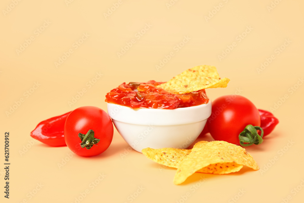 Bowl of tasty salsa sauce, vegetables and nachos on color background