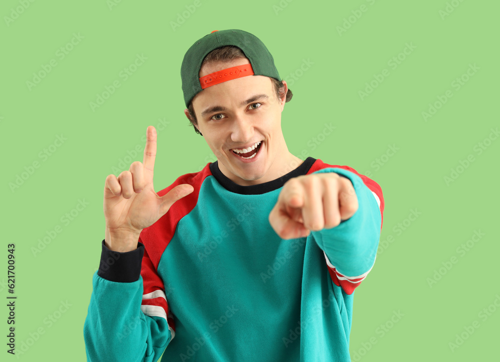 Young man showing loser gesture on green background