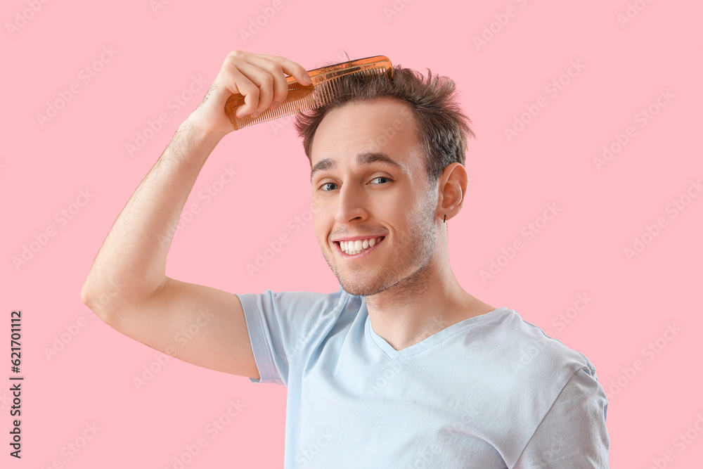 Young man combing hair on pink background