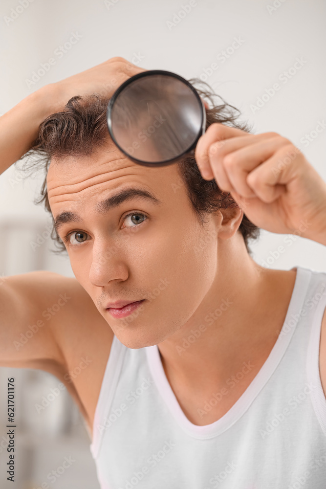 Young man with hair loss problem and magnifier in bathroom, closeup