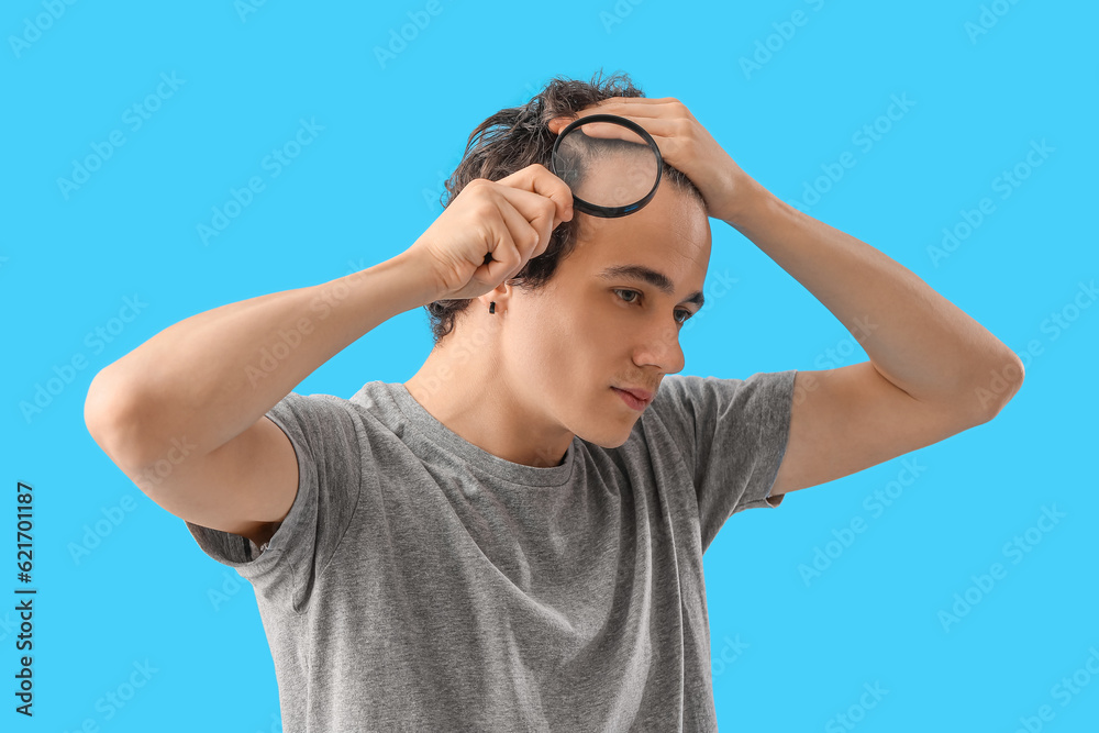 Young man with hair loss problem and magnifier on blue background