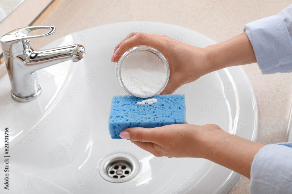 Woman cleaning white ceramic sink with baking soda, closeup