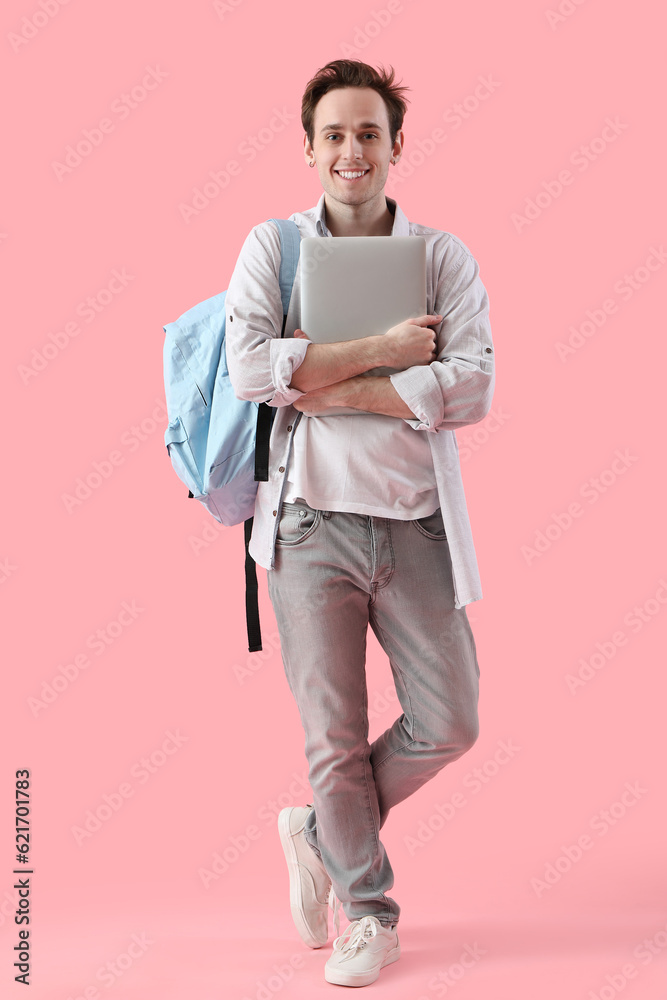 Male student with laptop on pink background