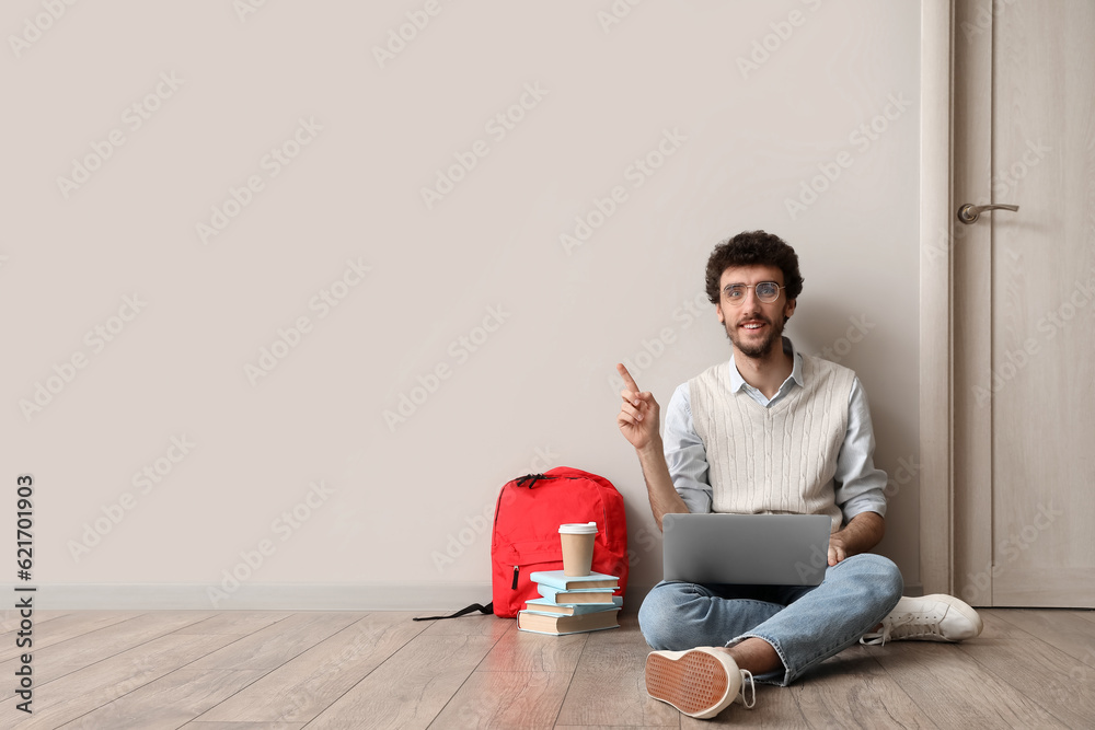 Male student with laptop pointing at something near light wall