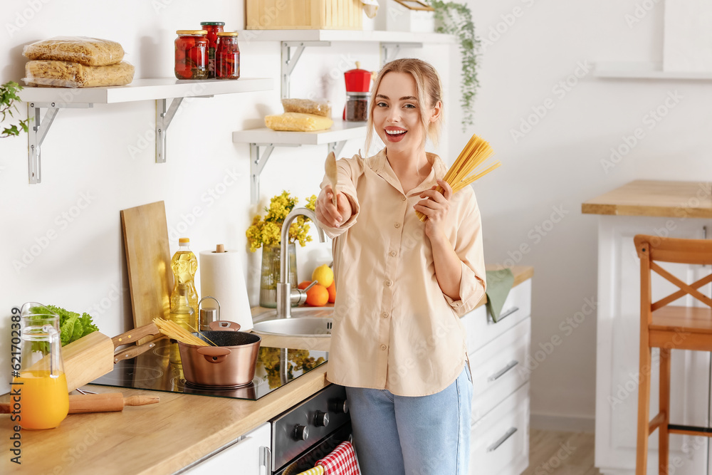 Young woman with raw spaghetti and spatula in kitchen