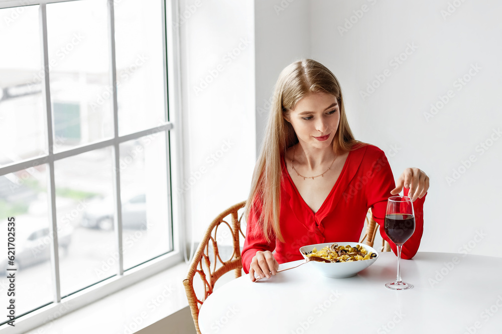 Young woman with glass of wine eating tasty pasta in restaurant