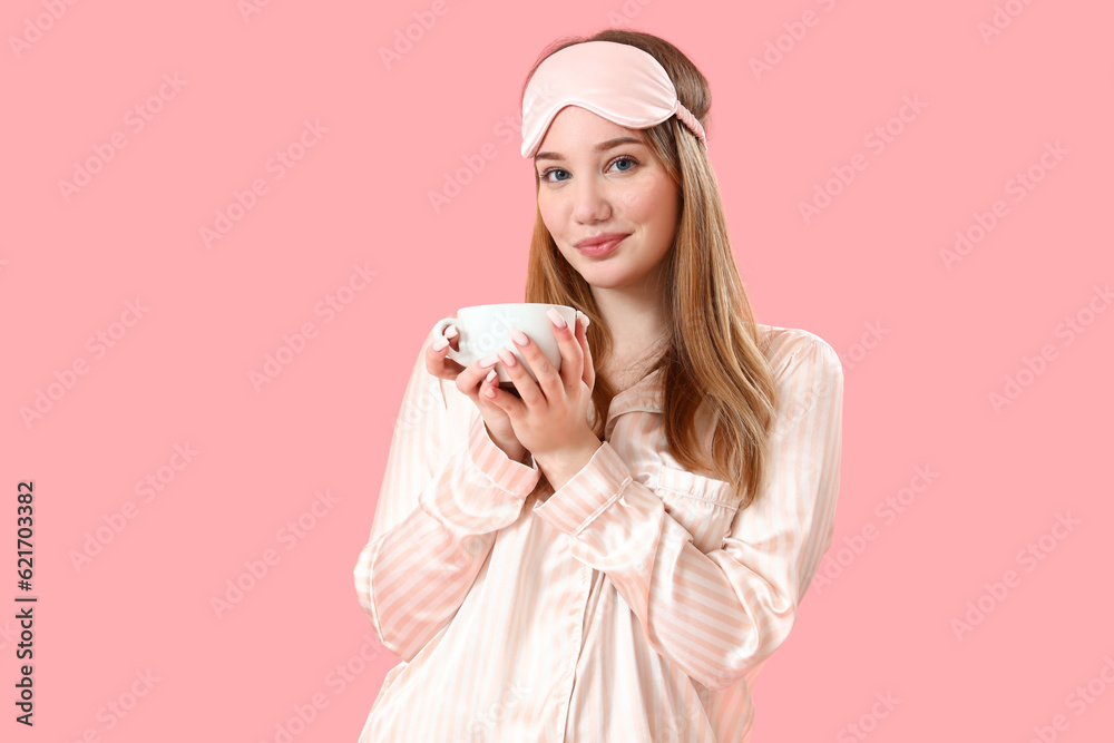 Young woman in pajamas with cup of coffee on pink background