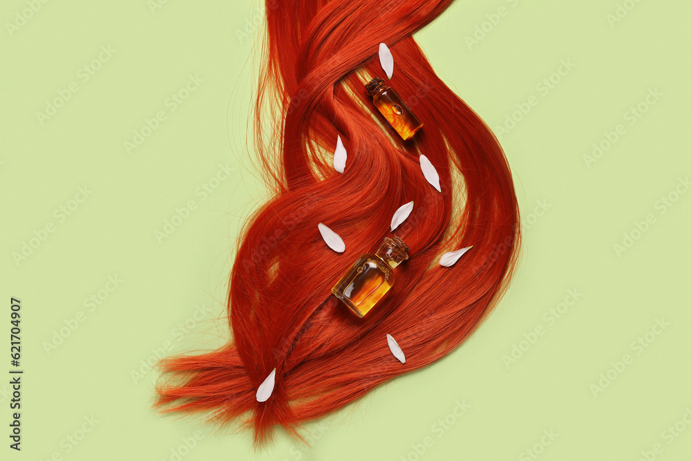 Composition with ginger hair strand, bottles of essential oil and flower petals on green background,