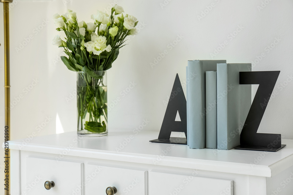 Bookend and vase with roses on table near light wall