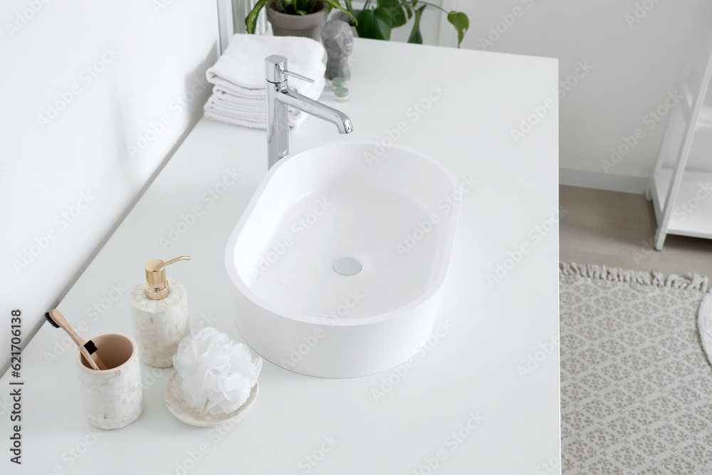 White sink and bath accessories on table in light bathroom