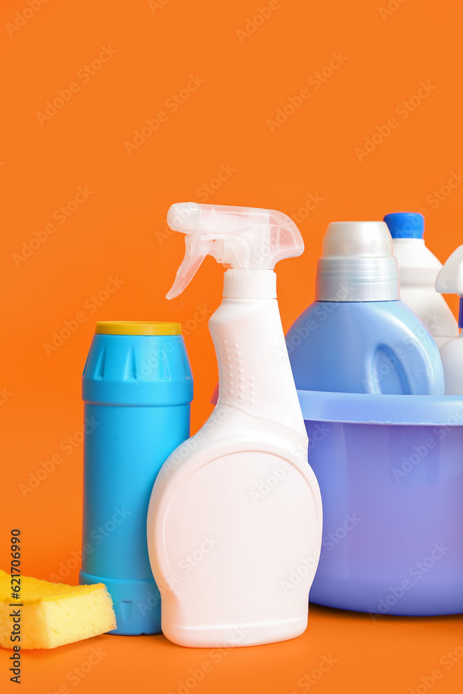 Bowl with different cleaning supplies on orange background