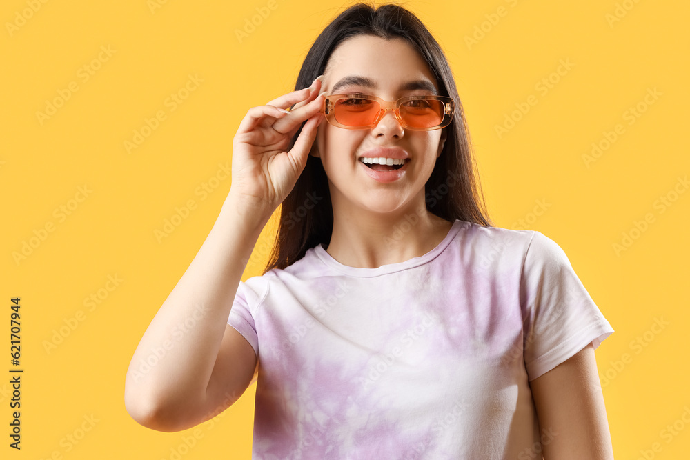 Beautiful young woman wearing stylish sunglasses on yellow background