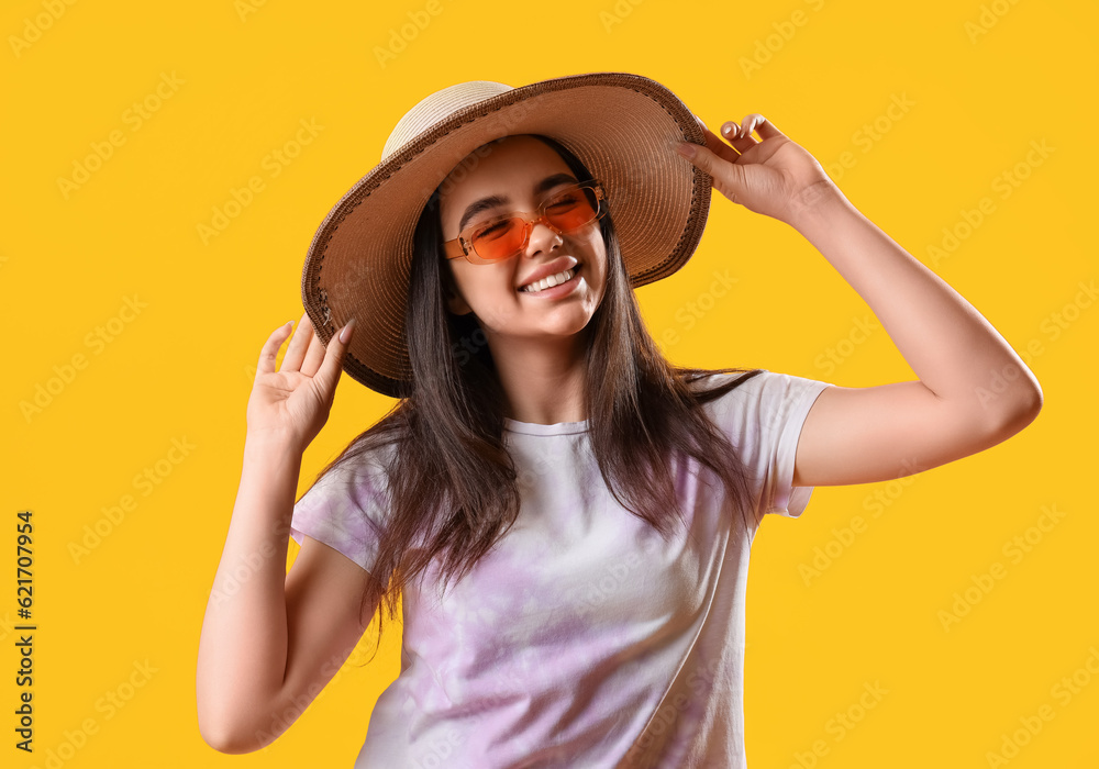 Beautiful young woman wearing stylish sunglasses and hat on yellow background