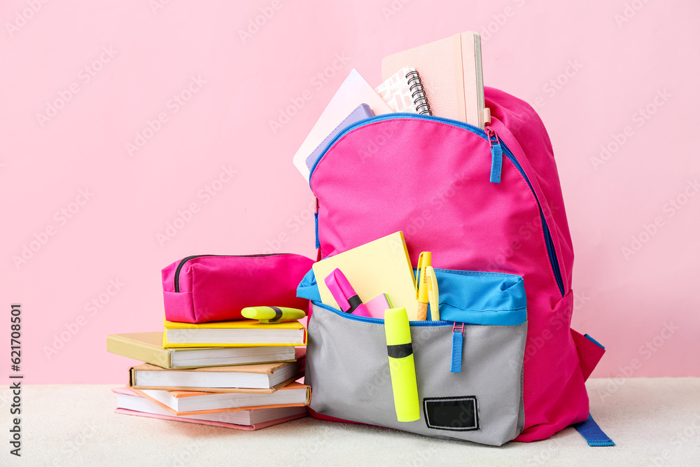 Pink school backpack with books, pencil case and markers on white table near color wall