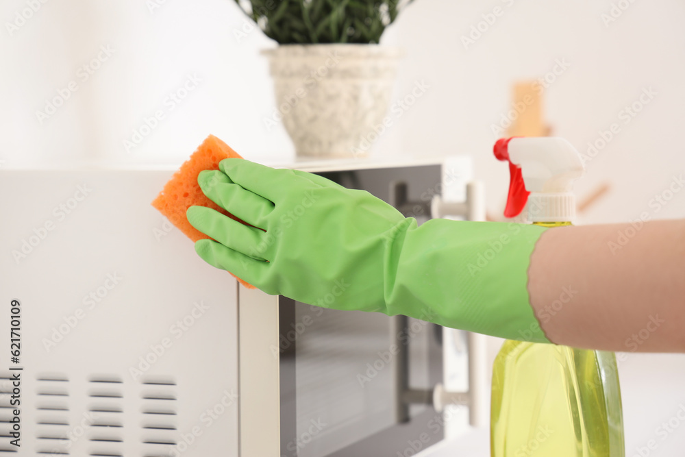 Woman cleaning microwave oven with sponge in kitchen, closeup