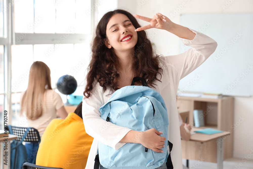 Female student with backpack showing victory gesture in classroom