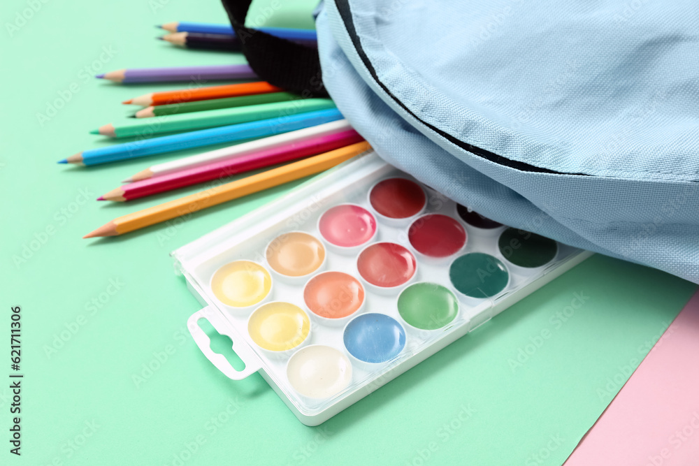 School backpack with different colorful pencils and paints on turquoise background, closeup