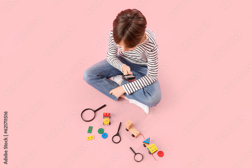 Little boy with magnifiers and toys on pink background