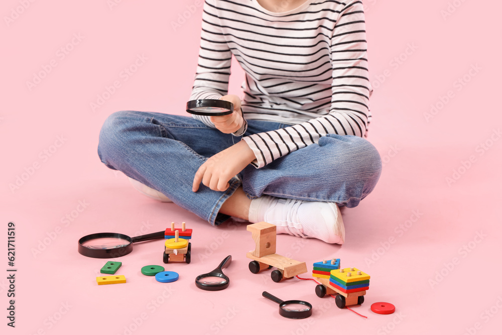 Little boy with magnifiers and toys on pink background