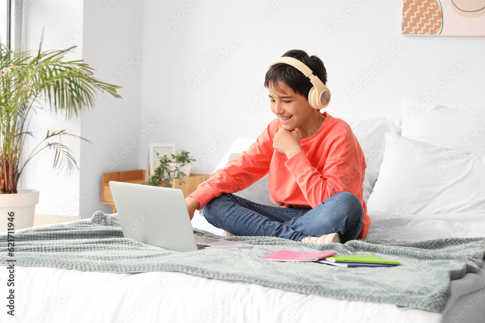 Little boy with headphones using laptop in bedroom