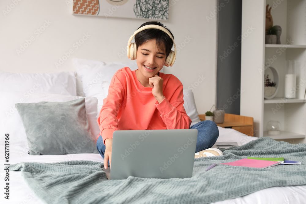 Little boy with headphones using laptop in bedroom