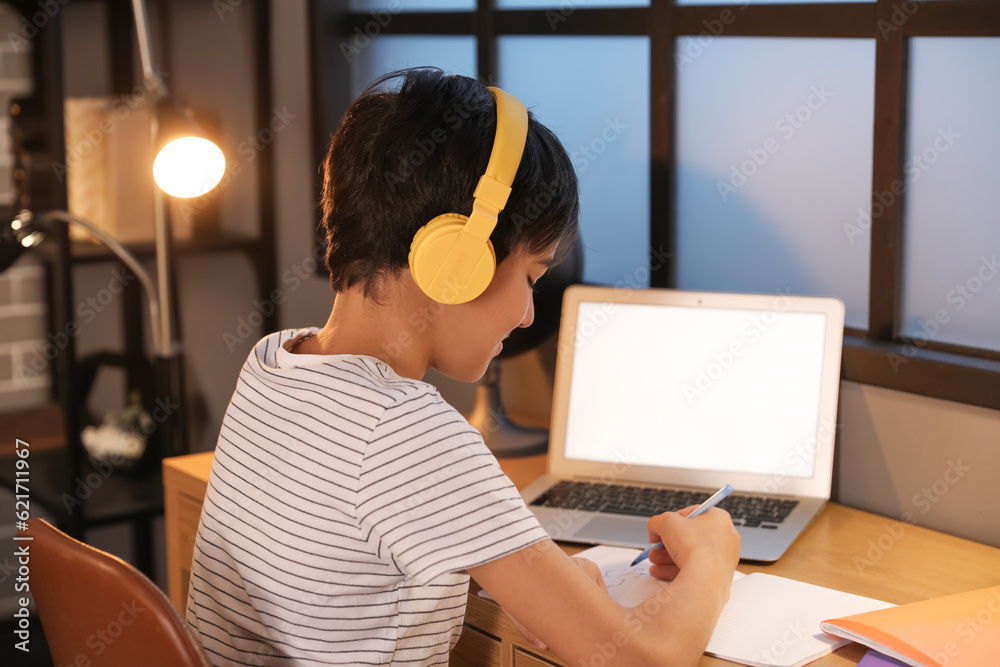 Little boy with headphones studying at home late in evening