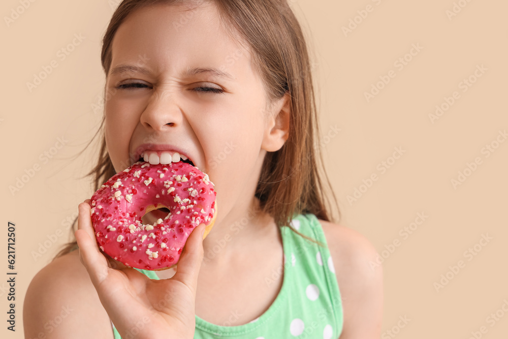 Angry little girl eating tasty doughnut on beige background, closeup