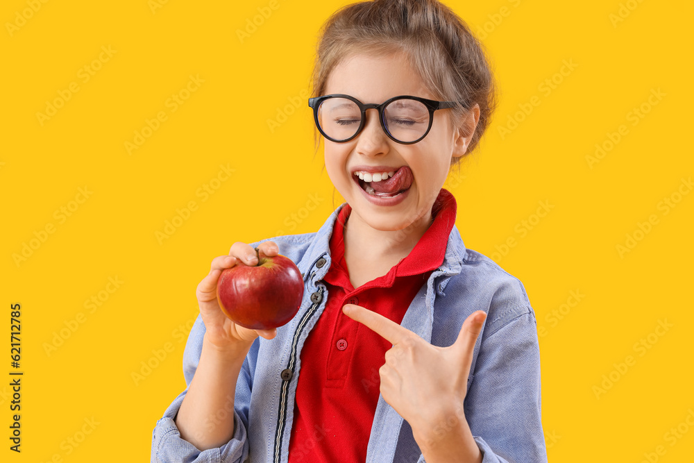 Little girl pointing at apple on yellow background