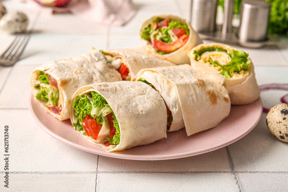 Plate of tasty lavash rolls with tomatoes, egg and greens on white tile background