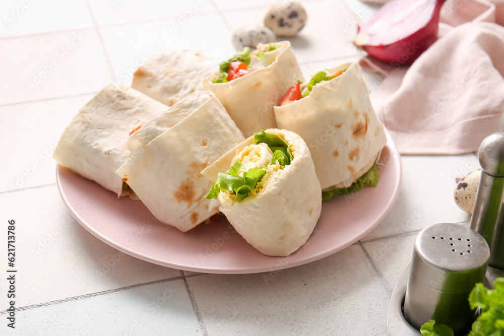 Plate of tasty lavash rolls with tomatoes, egg and greens on white tile background