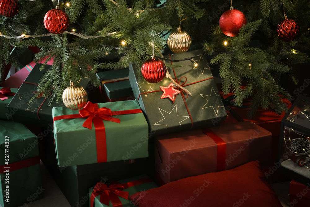 Gift boxes under Christmas tree with balls and glowing lights, closeup